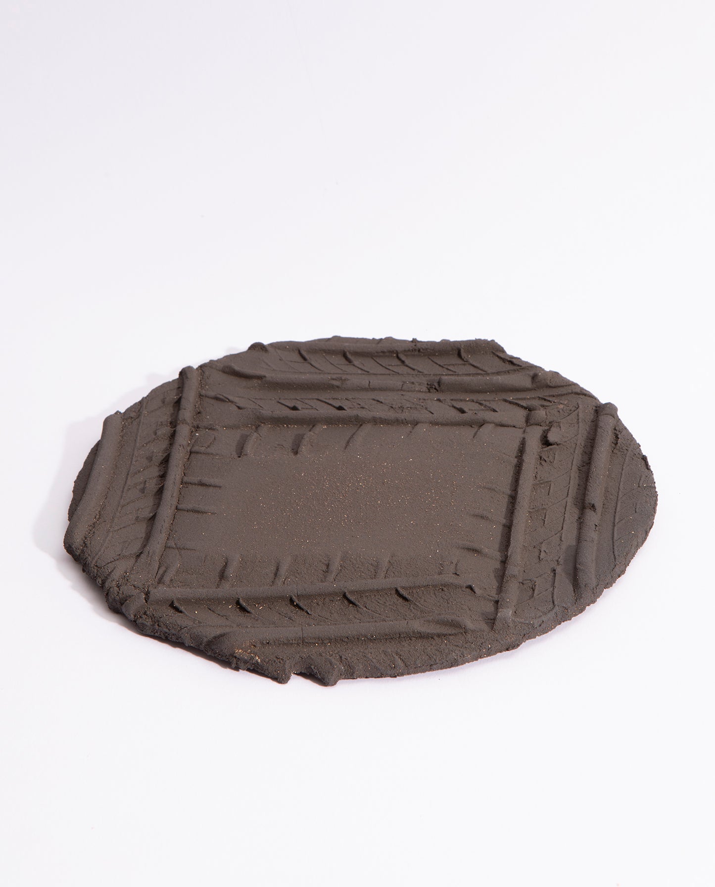 Assiette en grès noir brut, avec quatre empreintes de pneu qui forme un carré sur l'assiette.